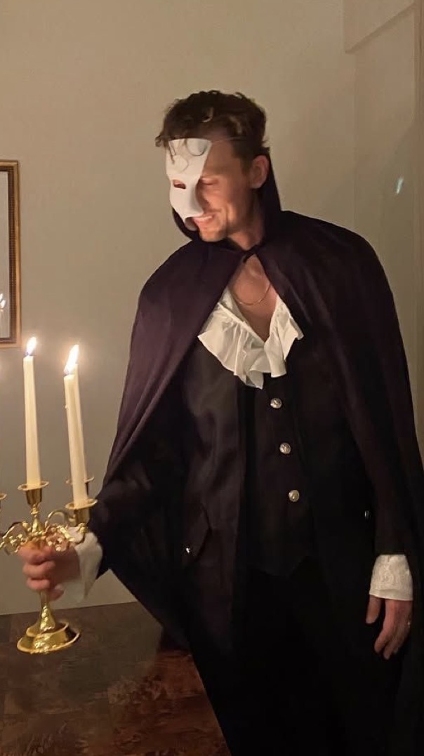 Mezza maschera, mantello scuro e camicia a balze accanto a un candelabro acceso