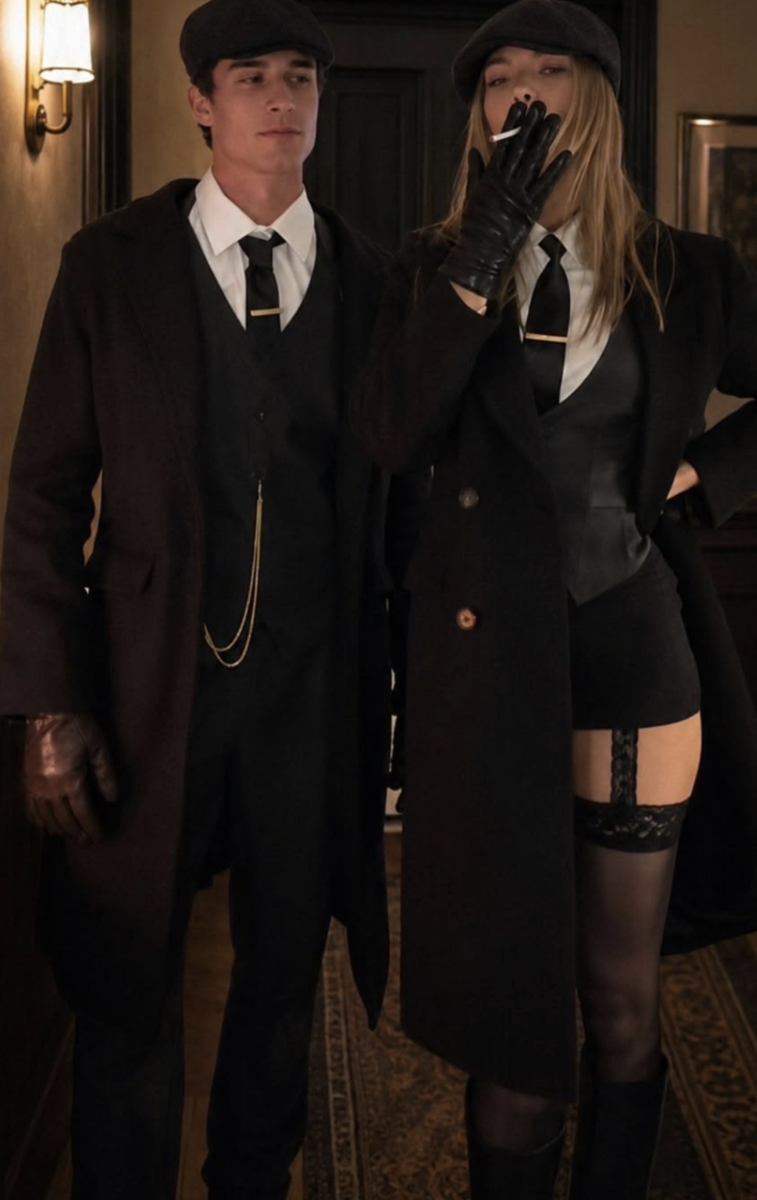 Coppia in cappotti lunghi, gilet e coppole in stile anni Venti